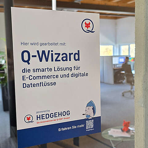 Auf einem Schild an einer Glaswand steht "Q-Wizard: die smarte Lösung für E-Commerce und digitale Datenflüsse" mit einem Cartoon-Igel und dem Firmenlogo von Hedgehog. Im Hintergrund ist ein Büro mit einer Person an einem Computer zu sehen.