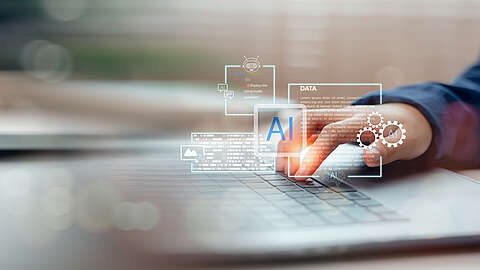 Die Hand einer Person tippt auf einer Laptop-Tastatur mit durchscheinenden digitalen Symbolen und Grafiken, darunter die Buchstaben "AI", die für künstliche Intelligenz und Datenanalysetechnologie stehen.