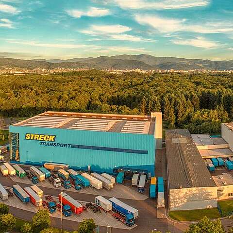 Luftaufnahme von "Streck Transport", im Vordergrund sind mehrere Gebäude mit großen Laderampen zu sehen, an denen zahlreiche LKWs und Anhänger geparkt sind. 
